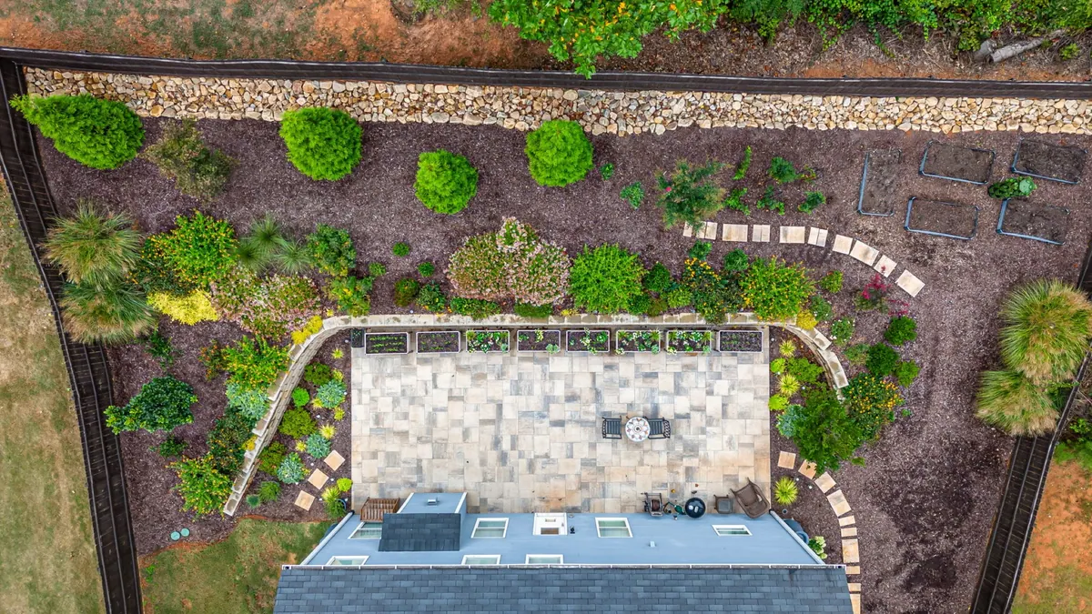 Aerial view of a complete GreenTree full-yard build: paver patio, curved retaining walls, and layered planting beds