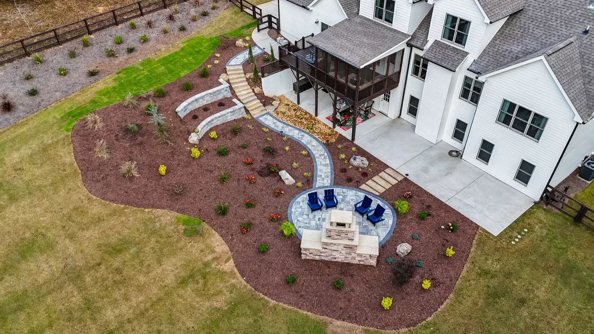 Aerial view of the finished landscape build: winding paver path, circular patio, and stone fireplace