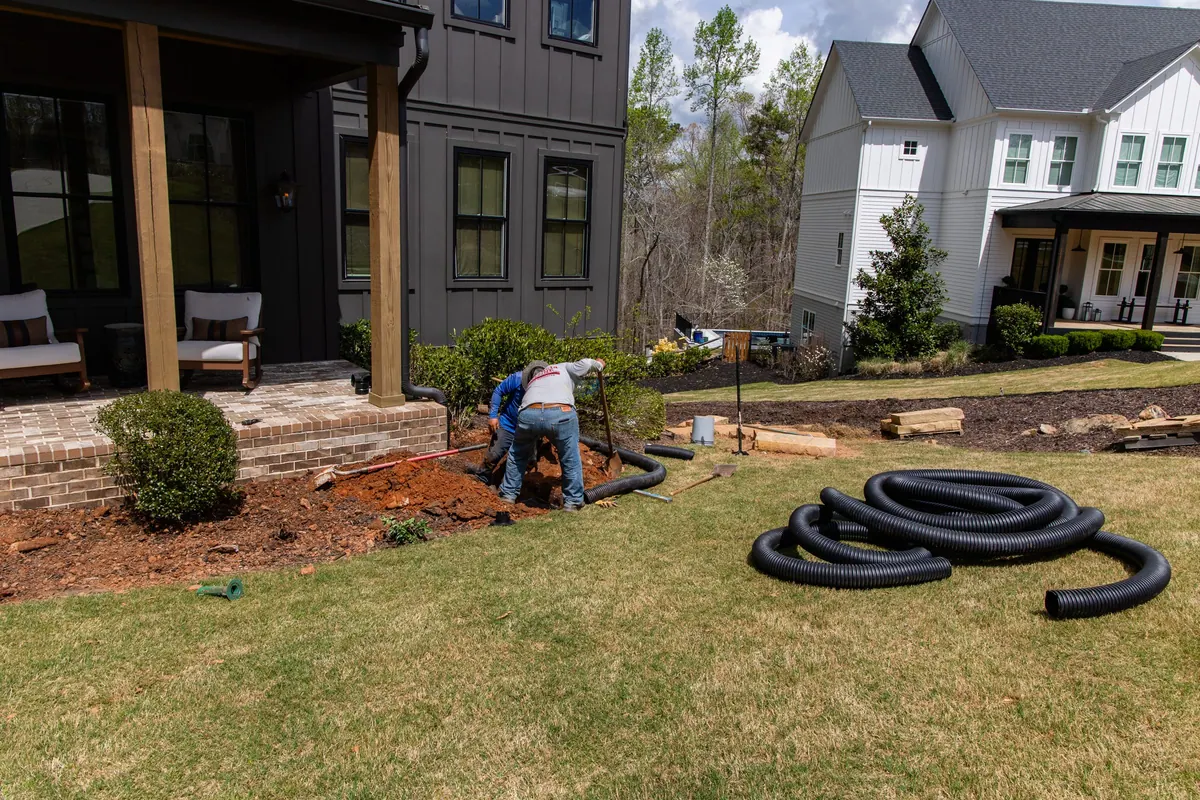 During: the crew burying downspout and drain lines along the foundation beds before hardscape went in
