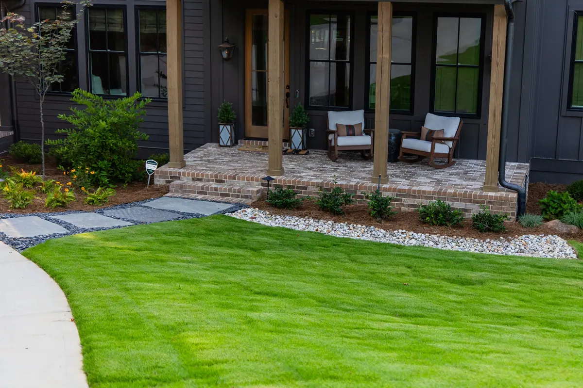 After: the refreshed front yard: porch, paver walkway, river-rock beds, and new sod