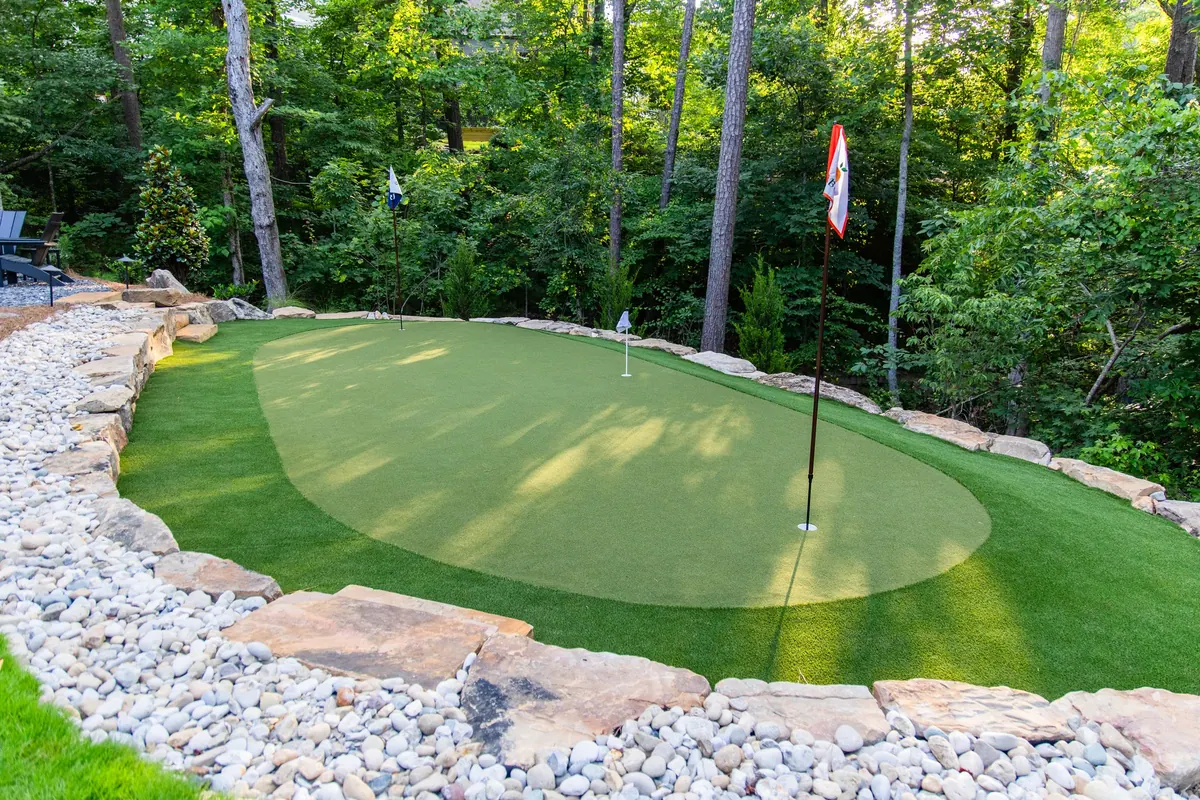 After: the putting green edged in river rock along the split-rail fence line