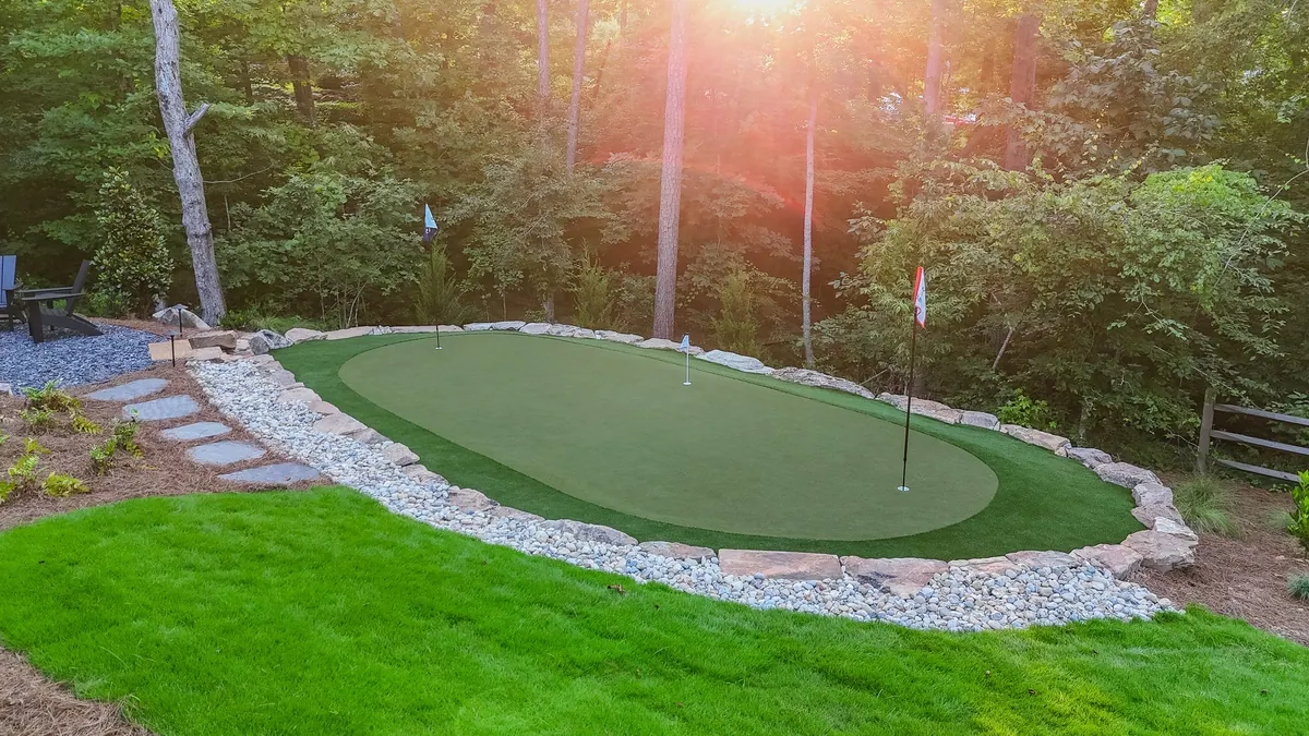 Backyard putting green, boulder retaining walls, and fresh lawn at sunset, the Blueberry Ridge project in Milton