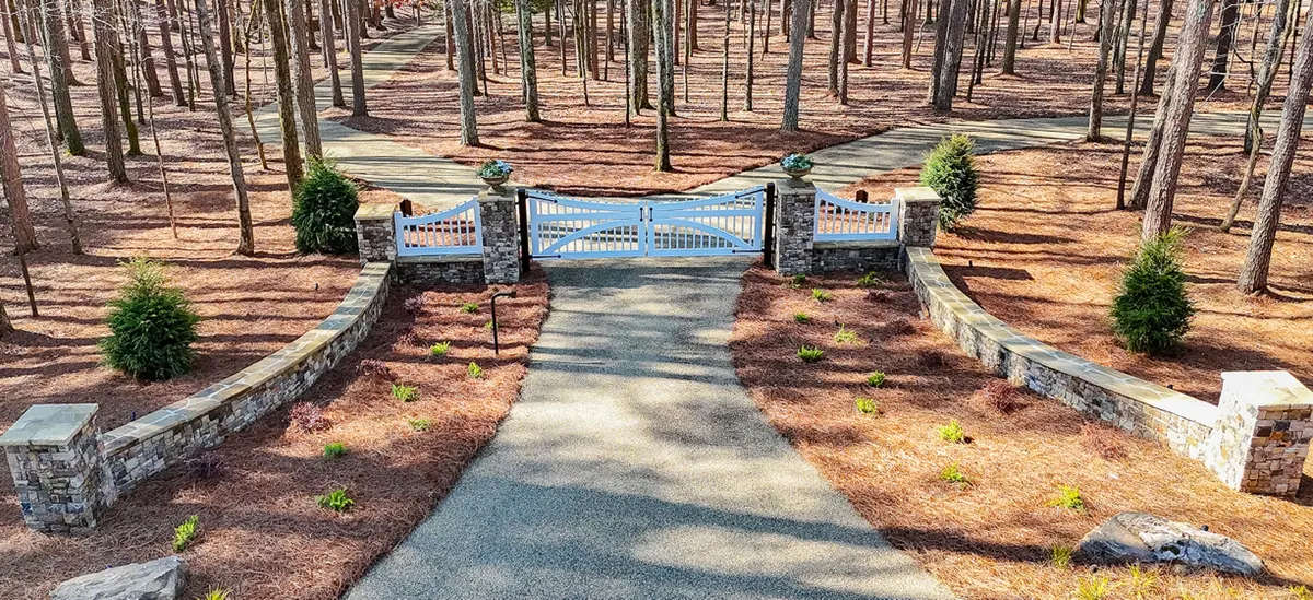 Custom white driveway gate with curved stacked-stone entrance walls and fresh plantings, built by GreenTree Landscapes