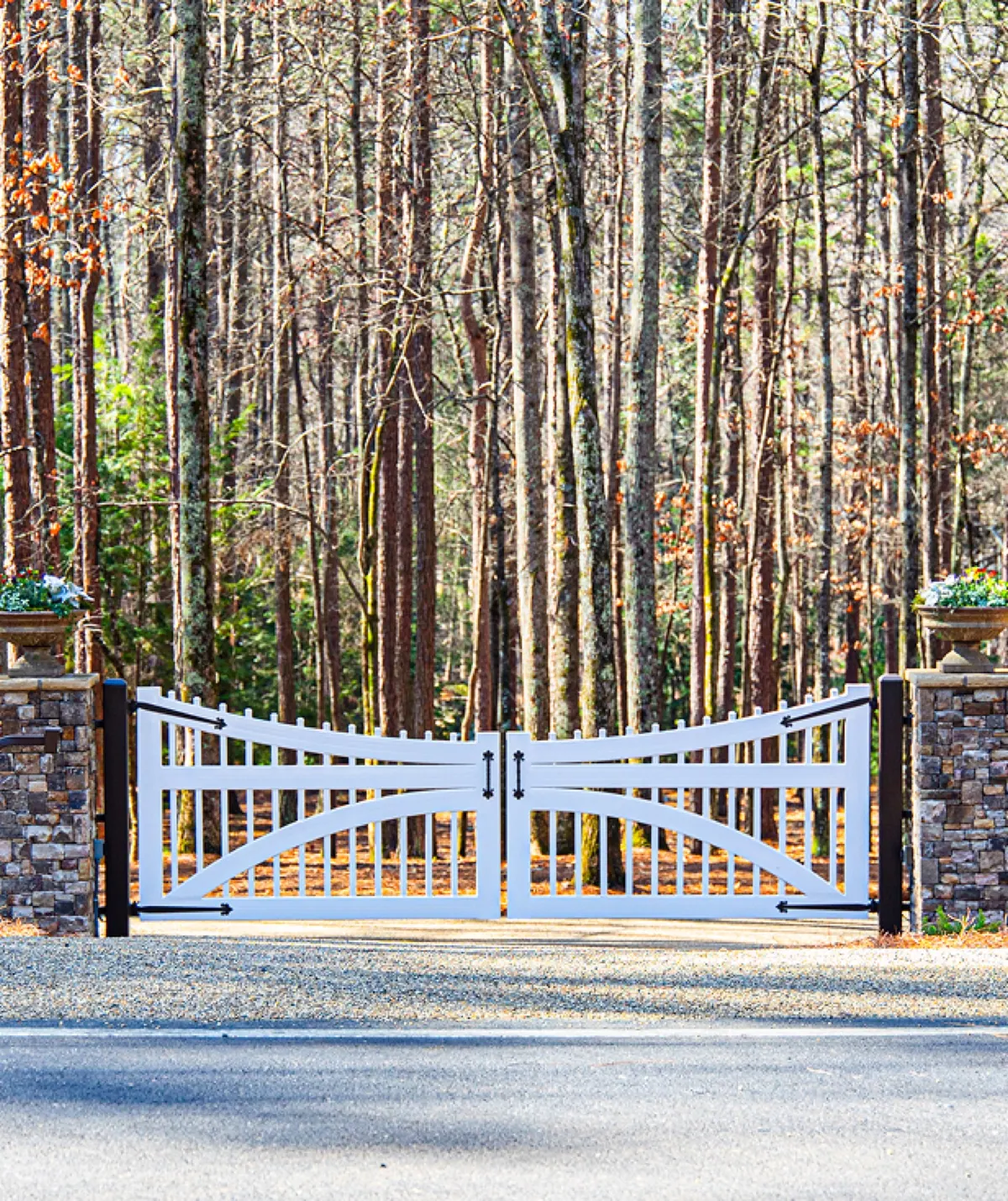 Custom white driveway gate between stacked-stone columns, seen from the street