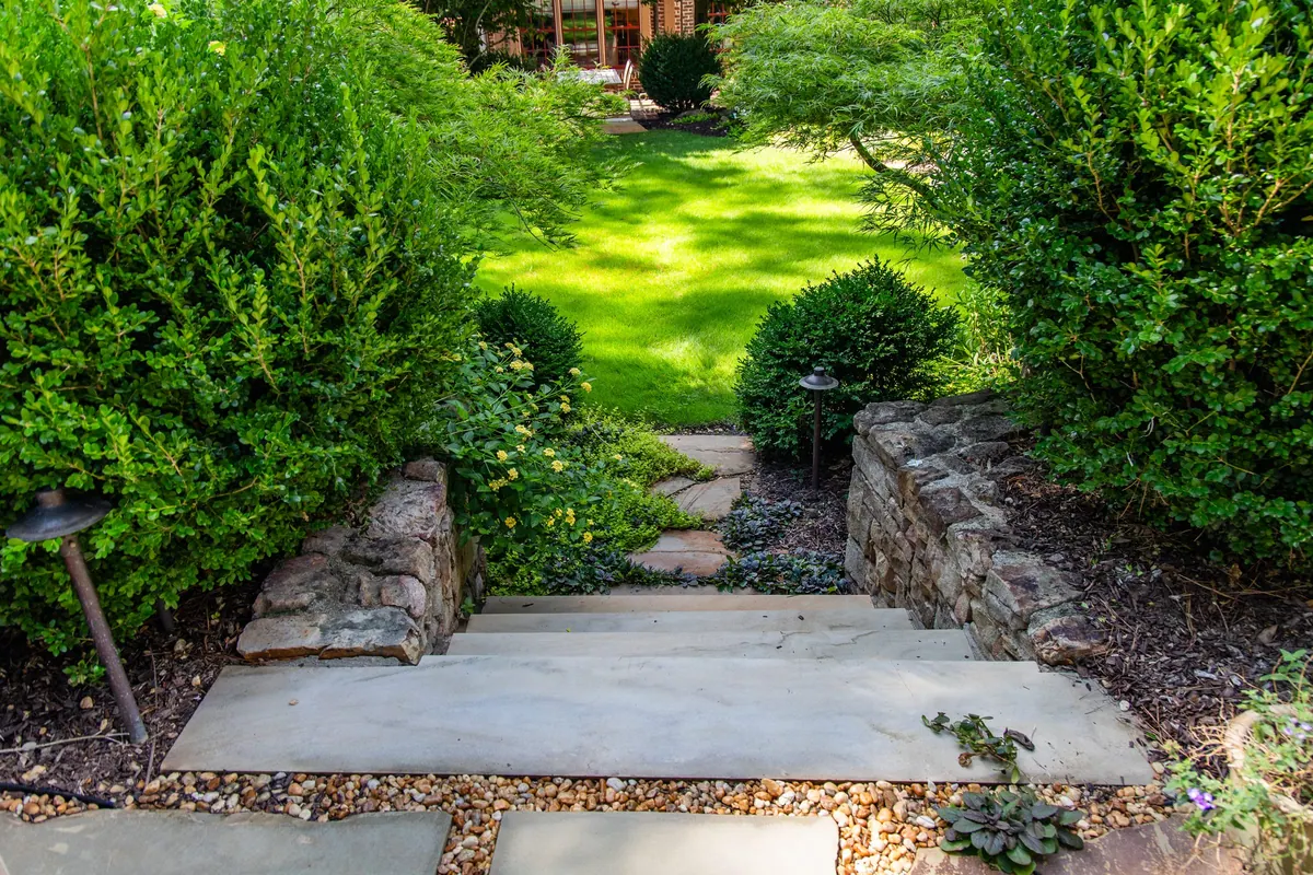 Stone slab steps between boxwood and stacked-stone walls up to the lawn