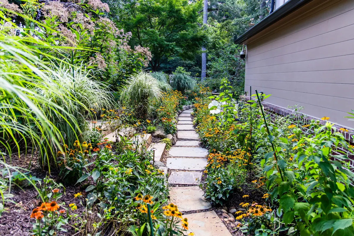 Stepping-stone path through black-eyed susans, coneflowers, and ornamental grasses in a GreenTree pollinator garden