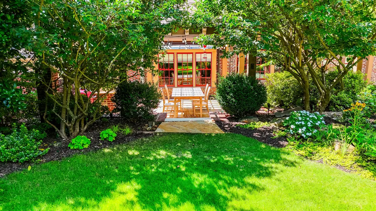 Established garden by GreenTree Landscapes: stone dining patio, clipped evergreens, and a lawn framed by mature planting beds