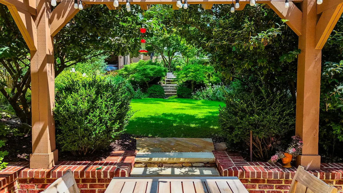View from under a timber pergola with string lights across brick columns to a manicured lawn, an established GreenTree garden
