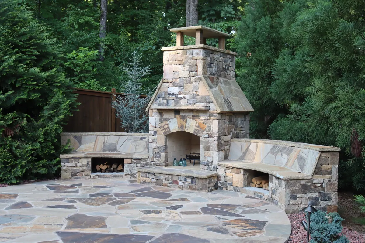 Stone outdoor fireplace with curved built-in benches on a flagstone patio by GreenTree Landscapes