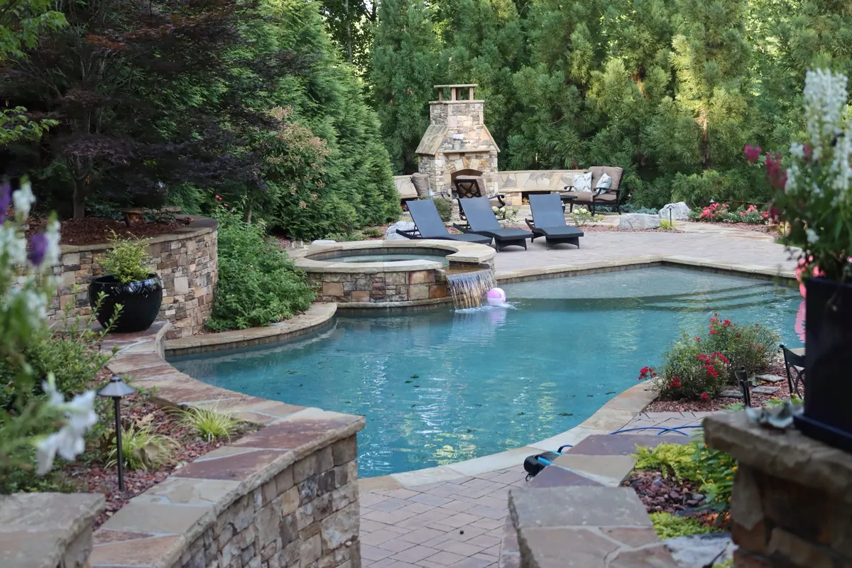 Stone spa and pool with an outdoor stone fireplace beyond, built by GreenTree Landscapes