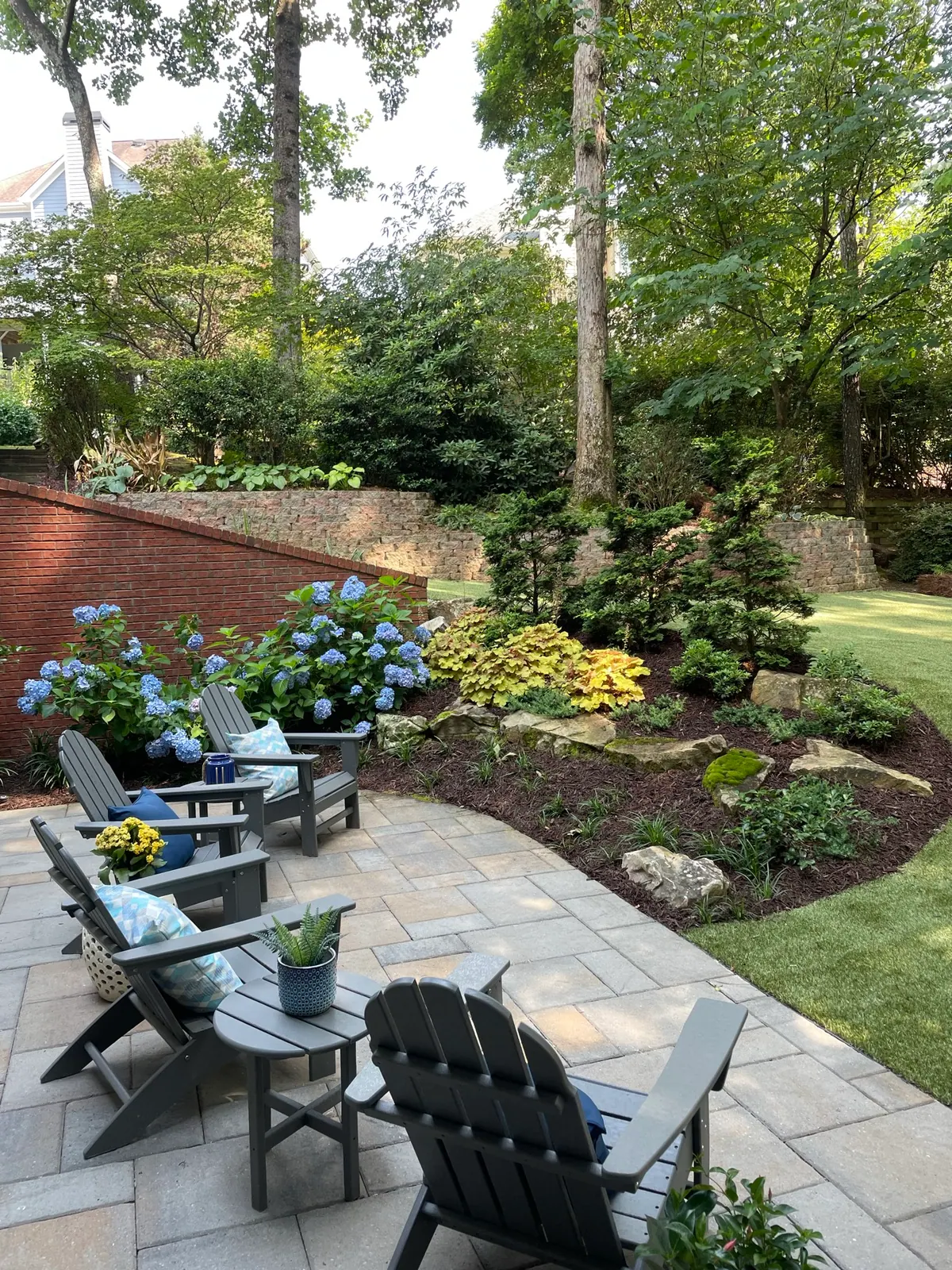 Paver patio with Adirondack seating, blue hydrangeas, and layered shade beds by GreenTree Landscapes