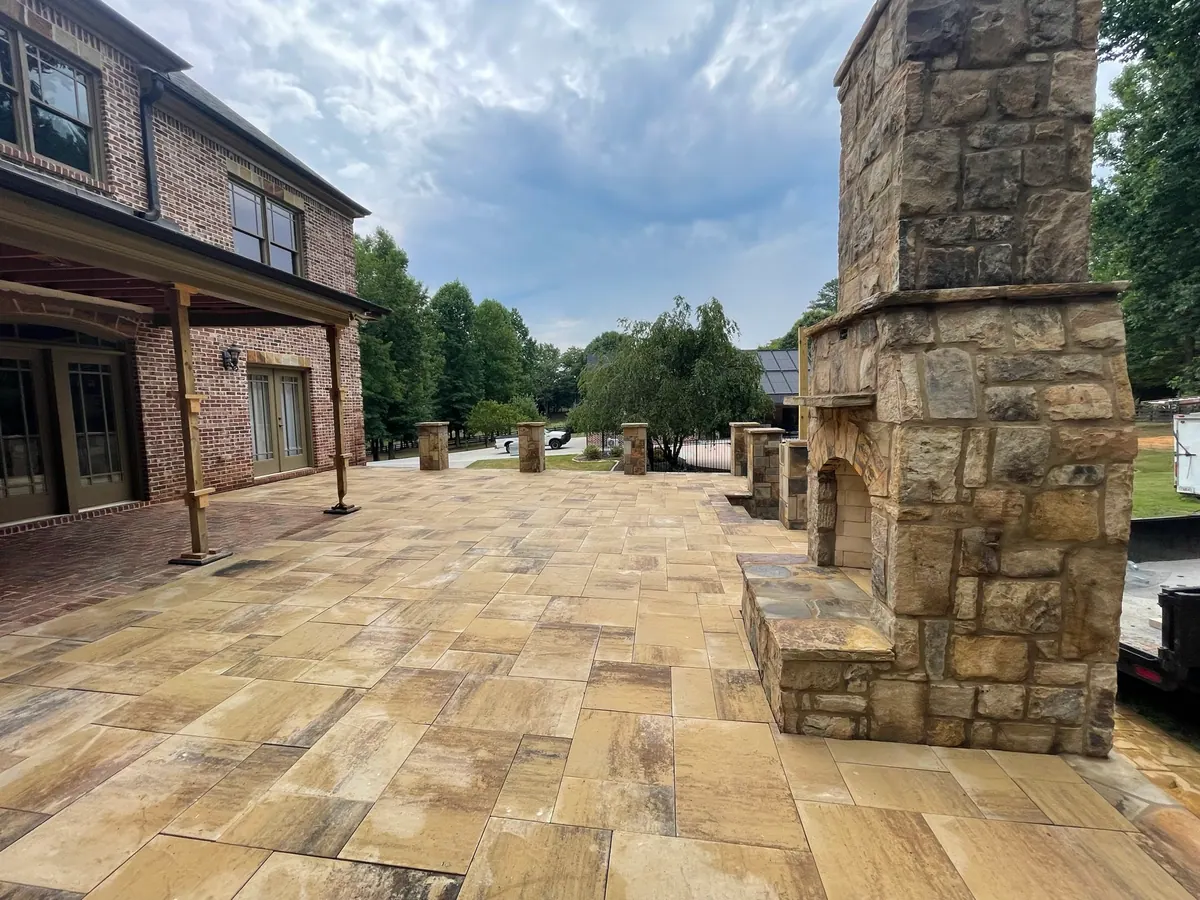 Travertine patio with a grand stone outdoor fireplace beside a brick home, GreenTree Landscapes build