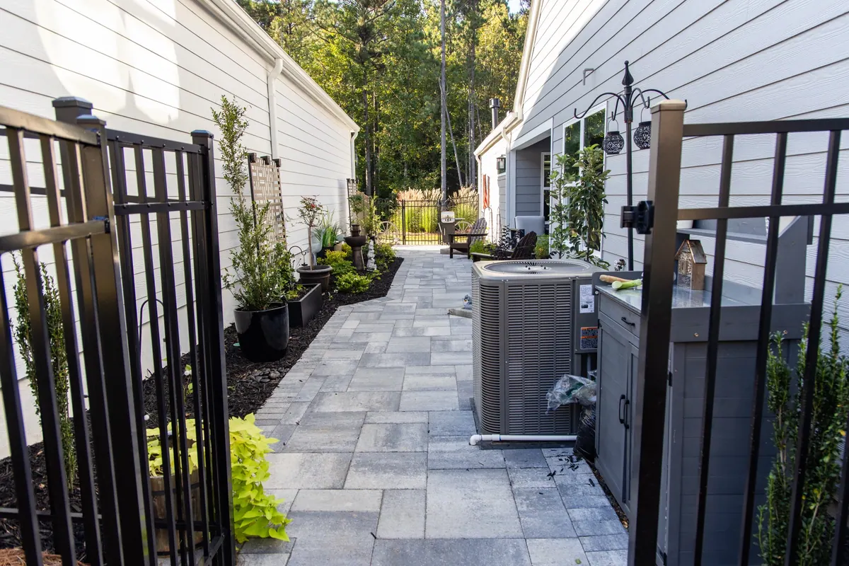 Side-passage hardscape with clean gray pavers, outdoor kitchen, and live green plantings against white siding, the Avery project by GreenTree Landscapes, Acworth, GA.